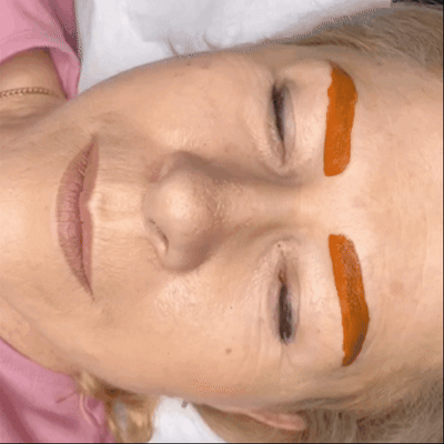 Bewegung einer Kundin mit einer roten Pigmentmaske, die ihre Augenbrauen bedeckt, um die Farbe zu erwärmen Bewegung einer Kundin mit einer roten Pigmentmaske, die ihre Augenbrauen bedeckt, um die Farbe zu erwärmen